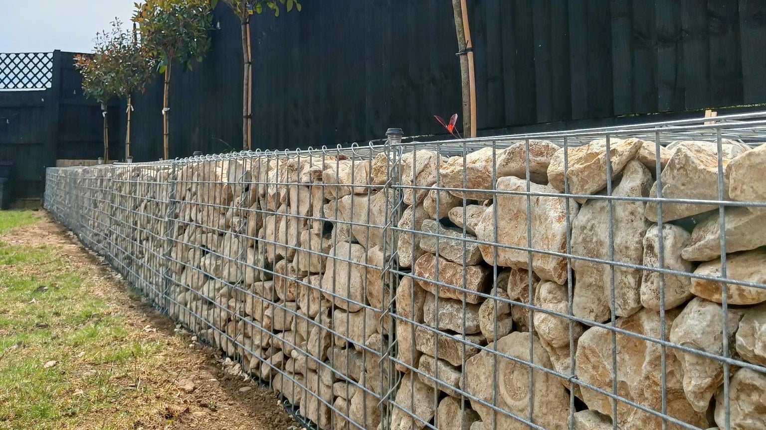 Gabion wall with trees and a wooden fence in the background